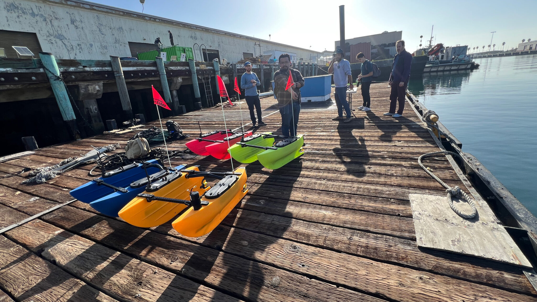A sophisticated BlueROV-style inspection robot equipped with a high-intensity LED light array and a precision gripper arm, performing a detailed survey of a subsea pipeline. The robot’s lights sharply illuminate the yellow-coated pipe and marine growth, while the surrounding deep water falls into a rich blue-green gradient. Tiny suspended particles catch the beams, adding realistic underwater texture. The camera is positioned slightly below and to the side of the ROV, capturing its silhouette against the lit pipeline. Photographic realism with a cinematic, focused mood that highlights accuracy, safety, and industrial subsea inspection capabilities in a clean, professional visual style.