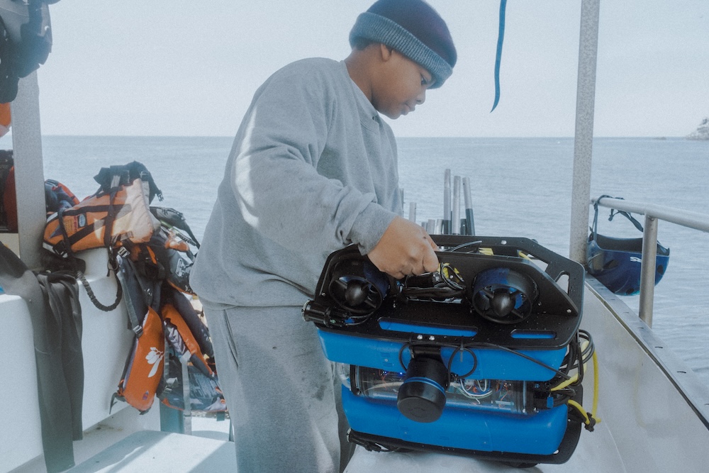 Student holding BlueROV2 sideways on a boat